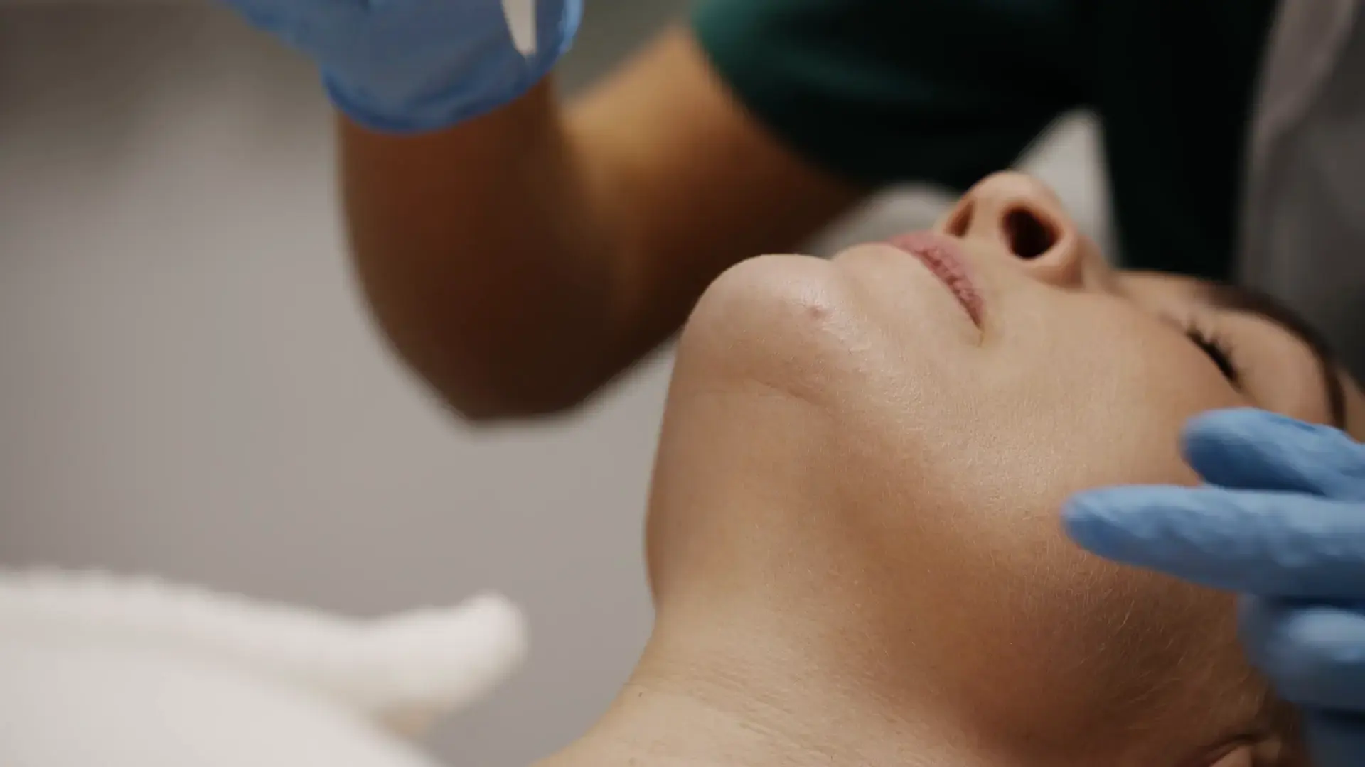 A practitioner's gloved hands support a client's chin during electrolysis